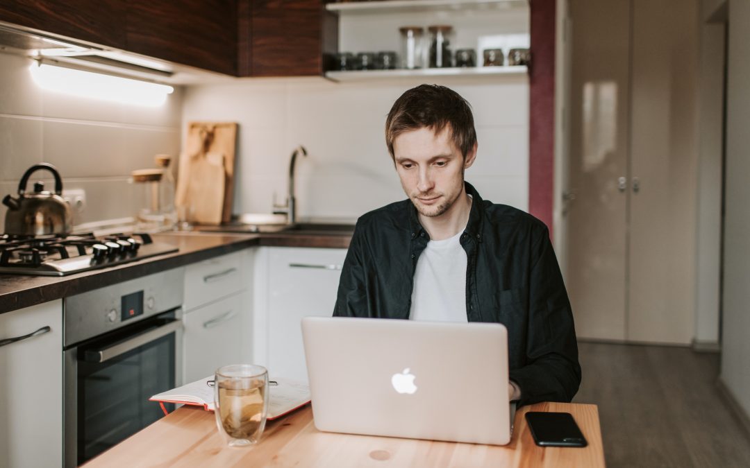 Mann sitzt am Küchentisch am Laptop und arbeitet