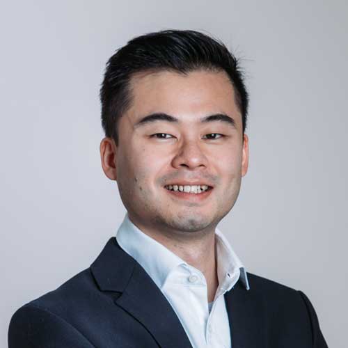 Liang Chen Porträt eines lächelnden Mannes mit kurzen, dunklen Haaren vor einem neutralen, hellen Hintergrund. Er trägt ein weißes Hemd und einen dunklen Anzug, was einen professionellen und gepflegten Eindruck vermittelt. Sein freundlicher Gesichtsausdruck strahlt Kompetenz und Offenheit aus.