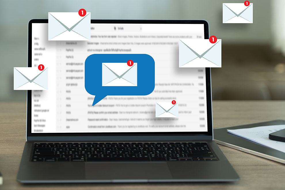 Nachrichten_990x660 Offener Laptop mit geöffnetem E‑Mail-Posteingang; darüber mehrere schwebende Brief‑Symbole mit roten Benachrichtigungs‑Badges – Symbol für neue Nachrichten und E‑Mail‑Benachrichtigungen im Büroalltag.