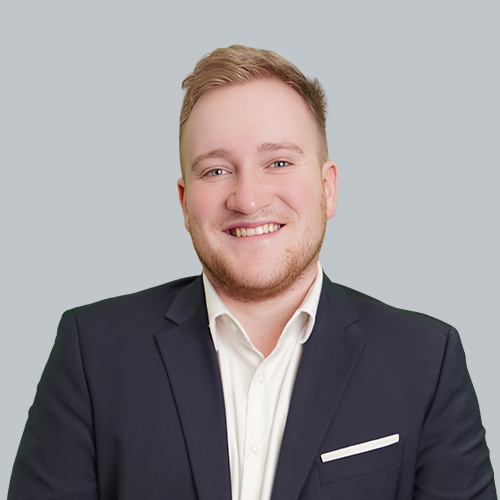 Porträt eines lächelnden jungen Mannes im Anzug mit weißem Hemd vor neutralem grauem Hintergrund – professionelles Business-Foto.