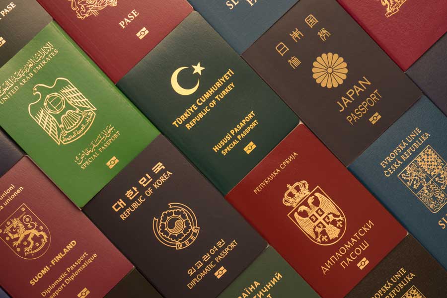 Mehrere Reisepässe verschiedener Länder nebeneinander und übereinander angeordnet, darunter Pässe aus den Vereinigten Arabischen Emiraten, der Türkei, Japan, Finnland, Südkorea, Serbien, Tschechien und weiteren Staaten in unterschiedlichen Farben wie Grün, Rot, Dunkelblau und Bordeaux, jeweils mit goldener Prägung des nationalen Wappens und Landesnamens.